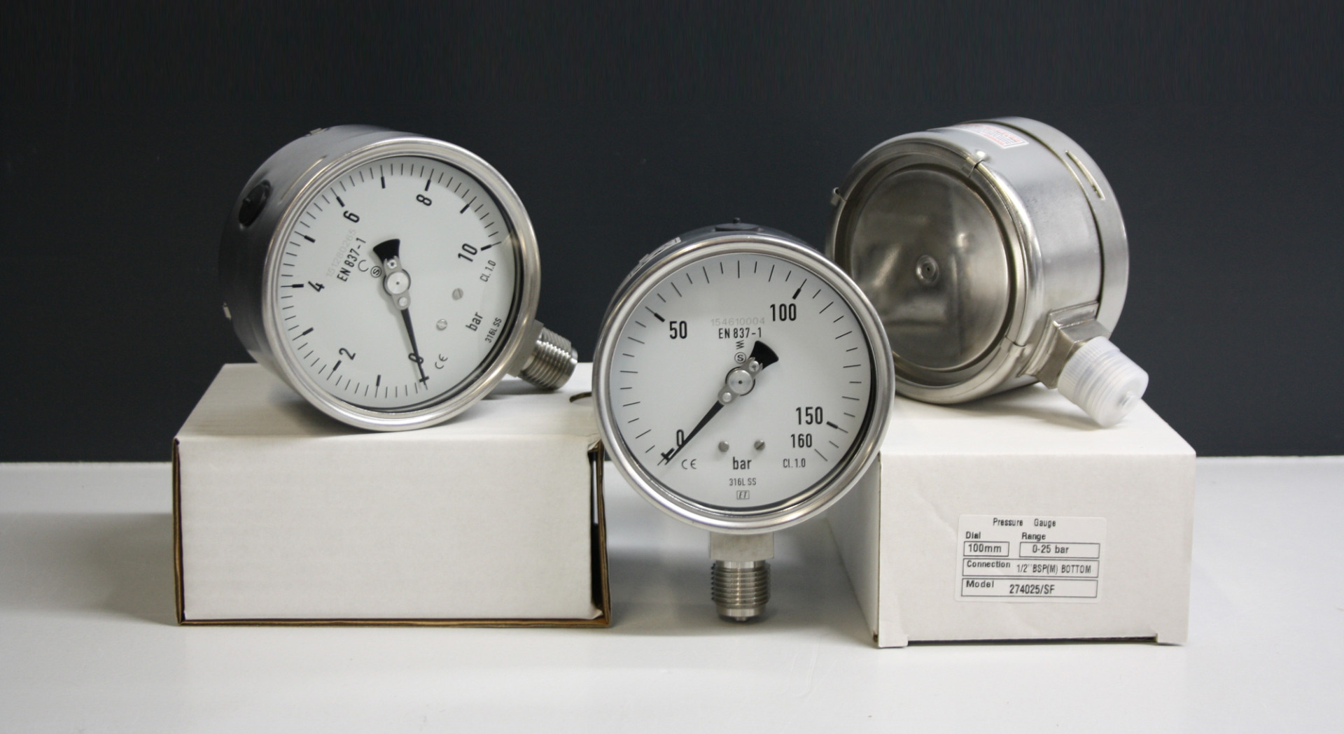 Drei verschiedene Hydraulikmanometer von 0 bis 160 bar, liegend auf Verpackung dargestellt